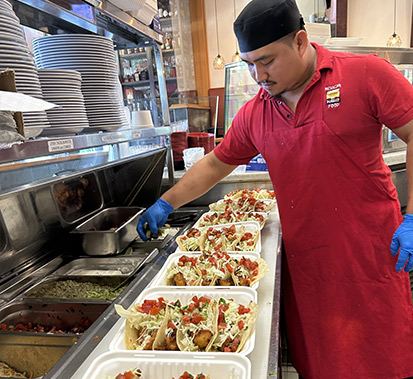 An El Pueblo chef plating a row of fresh fish tacos in the kitchen